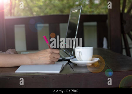 A woman write note on notebook and open laptop with coffee cup on wooden table. Stock Photo