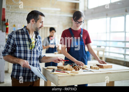 Carpenter giving advice to student in workshop Stock Photo