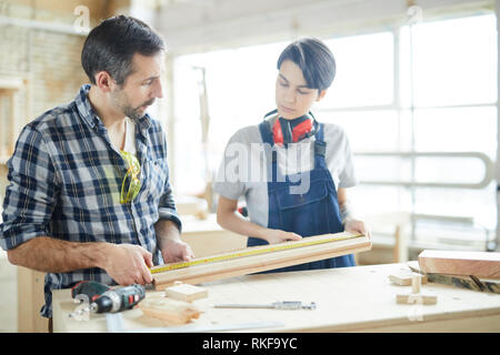 Carpenters checking measurement of wooden plank Stock Photo