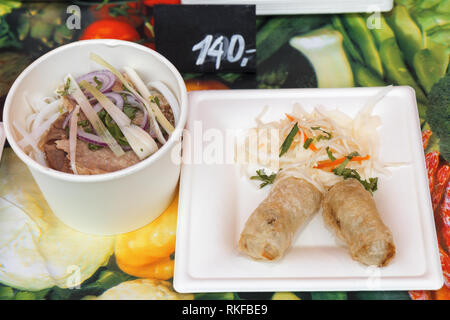 Asian street food, fried spring rolls with vegetable salad and Pho Bo soup, meat and vegetable food, traditional vietnamese soup, served in plastic di Stock Photo