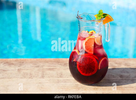 Glass jug of iced sangria with strawberry, orange, apple and lemon by the pool Stock Photo