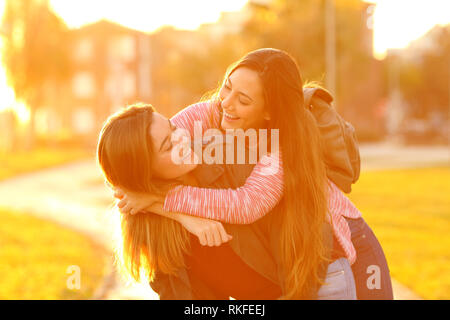 Two funny friends joking piggybacking in the street at sunset Stock Photo
