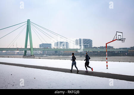 jogger on the Rhine riverbank in the district Deutz, the Severins bridge, in the background the Rheinau harbor, snow, winter, Cologne, Germany.  Jogge Stock Photo