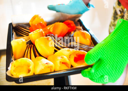 Close up shot of roast pepper and eggplant in a tray. A man is holding it in his hands wearing oven gloves. Party time Stock Photo