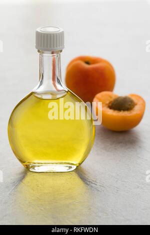 Glass bottle with cosmetic apricot kernel oil and fresh apricots on the background.