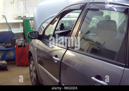 Gray color passenger car with opened hood undergoing repairs indoor in service station Stock Photo