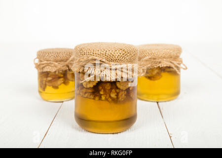 Walnut with honey in glass jars on white wooden boards. Delicious sweet delicacy. Stock Photo