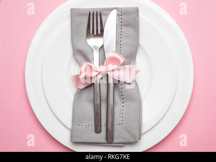 Table place setting in pink. Gray linen napkin with ribbon and white plates on pink color background, closeup top view, Stock Photo