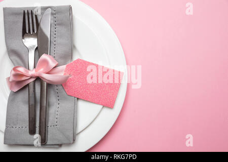 Table place setting in pink. Gray linen napkin with ribbon and blank tag on pink color background, closeup top view, copy space Stock Photo