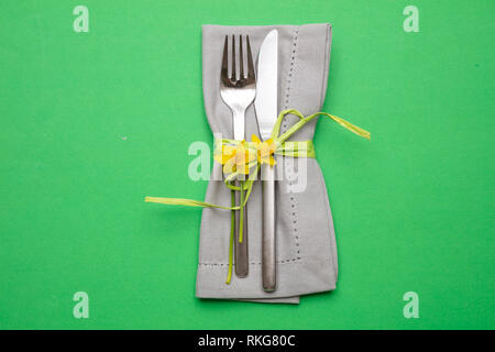 Table place setting in bright green. Gray linen napkin with decoration and cutlery on green color background, top view, Stock Photo