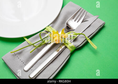 Table place setting in bright green. Gray linen napkin with decoration and white plate on green color background, close up view, Stock Photo