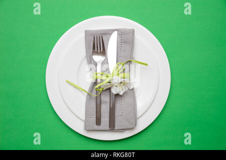 Table place setting in bright green. Gray linen napkin with decoration and white plates on green color background, top view, Stock Photo