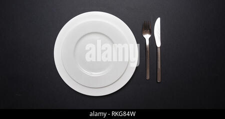 Table place setting on black. Set of empty white plates and cutlery on black color background, top view, copy space Stock Photo