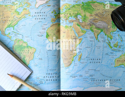 Lined Notebook with White Pencil and Camera on the World Map