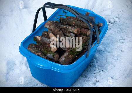 Wood for the fireplace in the blue, plastic basket on the snow. Firewood in a plastic basket Stock Photo