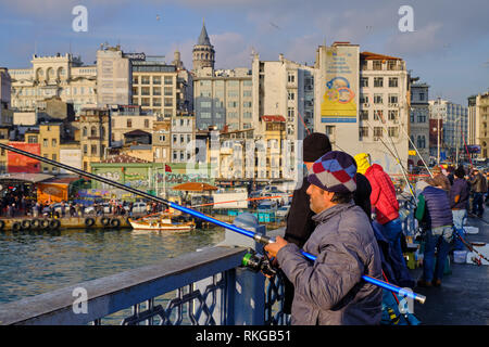 Focus on Fishermen on Galata bridge being lit by late afternoon sun.  Slopes of Karakoy and Galata Tower appear in the background. Istanbul, Turkey Stock Photo