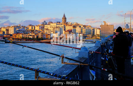 Fishermen on Galata bridge being lit by late afternoon sun.  Slopes of Karakoy and Galata Tower appear in the background. Istanbul, Turkey - December  Stock Photo
