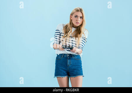 Beautiful concentrated blonde girl playing video games with joystick isolated on blue Stock Photo