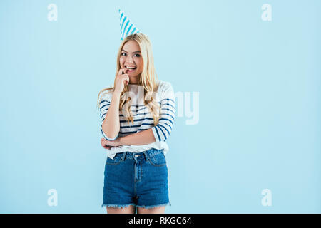 Girl in party hat biting finger isolated on blue Stock Photo