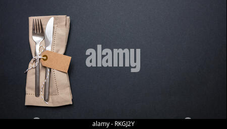 Business lunch, Table place setting with linen napkin and blank tag on black color background, banner, top view, copy space Stock Photo