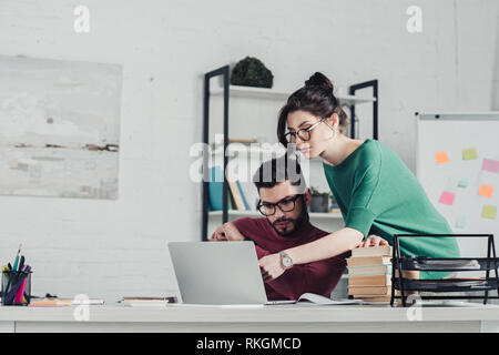 attractive woman pointing with finger at laptop near man in modern office Stock Photo