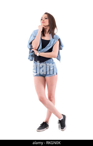 Thoughtful young woman in denim shorts and jeans jacket thinking and looking away. Full body isolated on white background. Stock Photo