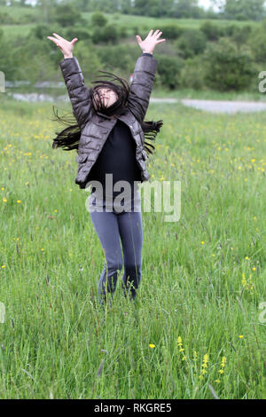 Adorable little girl jumping and having fun on meadow background Stock Photo