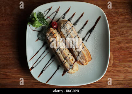 Two sweet french eclairs on plate. Breakfast in cafe. wooden table background Stock Photo