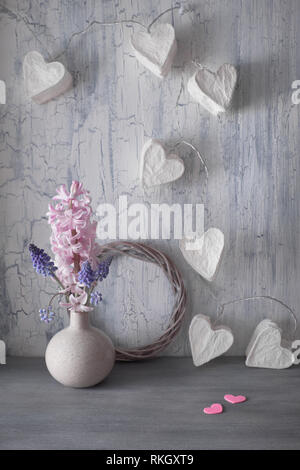 Valentines day or Springtime celebration, vase with hyacinth flowers and garland lights in shape of paper hearts on rustic background Stock Photo