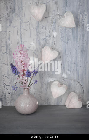 Valentines day or Springtime celebration, vase with hyacinth flowers and garland lights in shape of paper hearts on rustic background Stock Photo