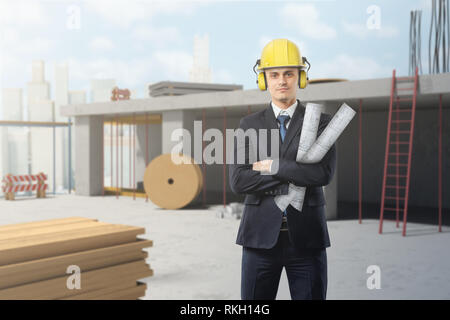 Young businessman wearing yellow safety helmet and holding blueprints at construction site Stock Photo