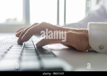 Low angle closeup view of businessman typing on computer keyboard with bright office windows in background. Stock Photo
