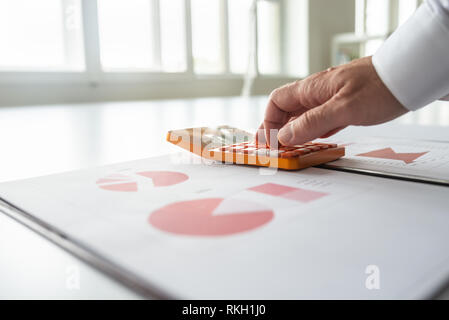 Closeup of financial advisor using calculator as he reviews statistical graphs and charts. Stock Photo