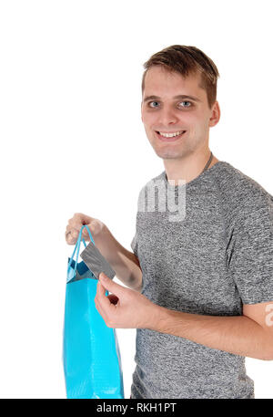 A young happy man standing in a gray shirt and holding his blue shopping bag and a credit card, isolated for white background Stock Photo