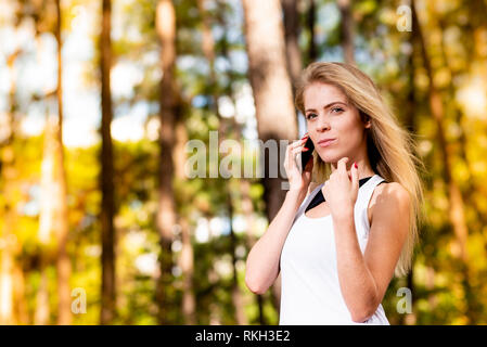 Beautiful blonde model in gym clothes talking on cellphone. Blurred forest background at sunset Stock Photo