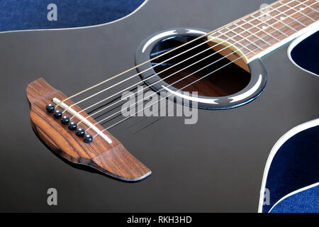 Classic acoustic six strings guitar black color top with cutaway fragment on jeans background side view closeup Stock Photo