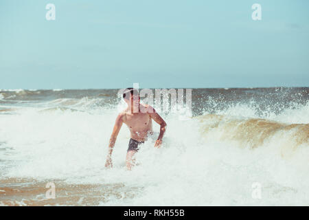 Young man enjoying the high waves in the sea during a summer vacations. Spending a summer holiday by the sea Stock Photo