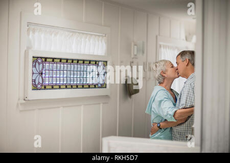 Affectionate mature couple share a tender kiss in the kitchen. Stock Photo