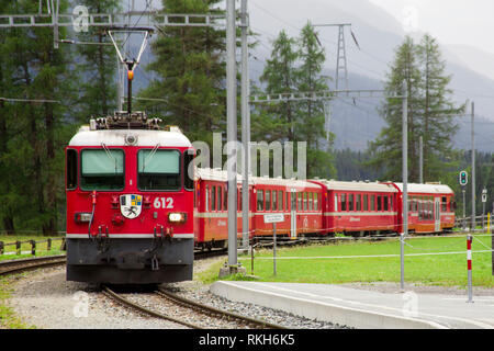 The train pulls up to the station of the old narrow-gauge railway in the valley of the Alpine mountains among the trees in cloudy weather. Stock Photo