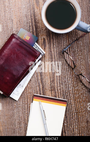 Leather wallet with dollar banknotes, credit card and receipt, glasses, cup of coffee on wooden desk. Portrait orientation Stock Photo