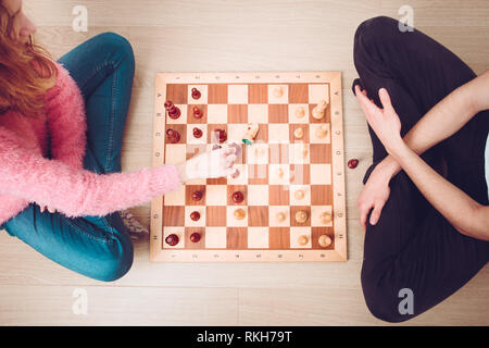 Girl and boy playing chess at home. Girl moving her piece and capturing her opponent's knight. Teenagers sitting on a floor. View from above. Copy spa Stock Photo
