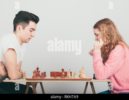 Girl and boy playing chess at home, they are concentrated on their next moves. Teenagers sitting by a table. Profile view. Copy space for text in the 