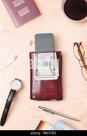 Wallet, dollar banknotes, smartphone, passport, earphones on the wooden desk. Tourist essentials. Things related to travel. Portrait orientation Stock Photo