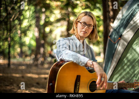 Mid adult woman playing guitar while camping. Stock Photo