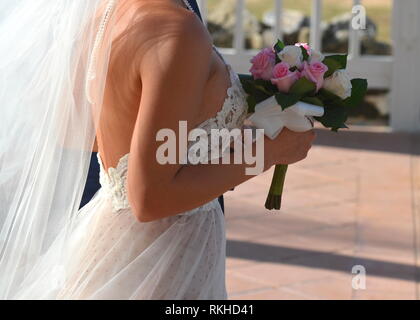 Young bride in a white lace halter top wedding dress walking down the aisle at a tropical resort hotel. Destination wedding in a tropical garden. Stock Photo