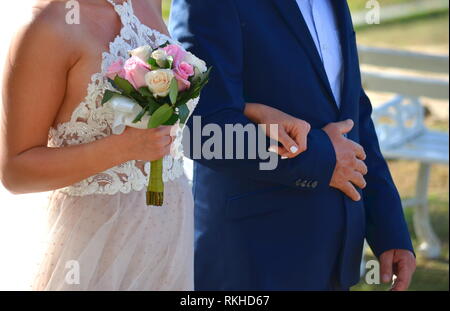 Young bride in a white lace halter top wedding dress walking down the aisle at a tropical resort hotel. Destination wedding in a tropical garden. Stock Photo