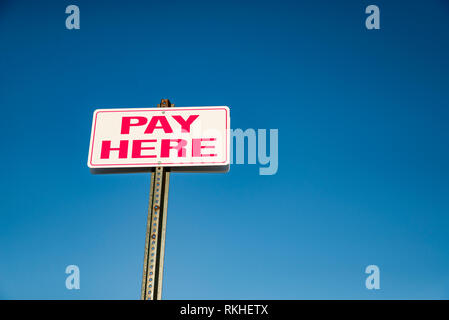 Pay Here signboard on top of an exterior wall with parked cars Stock Photo