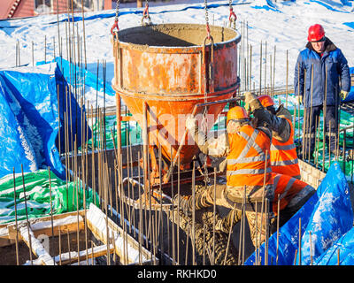 Workers use concrete bucket pouring wet concrete into formwork. Snow covers building construction on the background Stock Photo