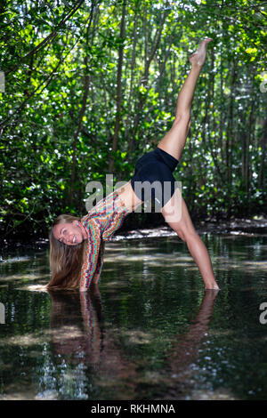 Young woman practicing yoga (Downward Facing Dog Split (Three-Legged Dog) in a natural setting - Fort Lauderdale, Florida, USA Stock Photo