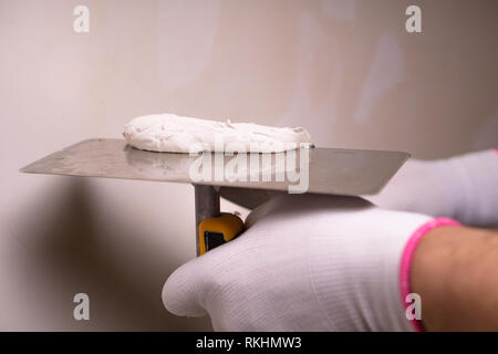 Hand with putty knife repair wall, Hand with a spatula, spatula with spackle paste structure, process of applying layer of putty trowel, working with  Stock Photo